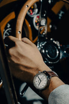 Driver’s watch OURO RW-002 équipée du Bracelet Grand Tourisme au poignet d’un conducteur tenant le volant en bois de sa voiture de collection.