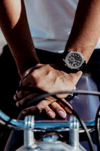 Montre OURO RW-001 avec le bracelet en cuir noir au poignet d’un motard les mains croisées appuyé sur le réservoir de sa moto de collection.