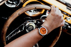 Montre OURO RW-003 avec bracelet en cuir noir portée au poignet, main posée sur le volant en bois d’une voiture classique.