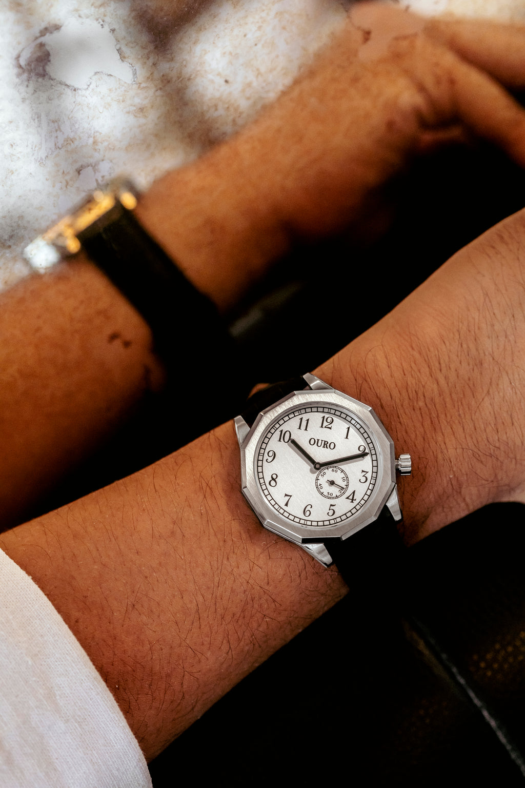 Montre OURO RW-002 avec bracelet en cuir noir portée au poignet, se reflétant dans un miroir dans un cadre vintage et élégant.