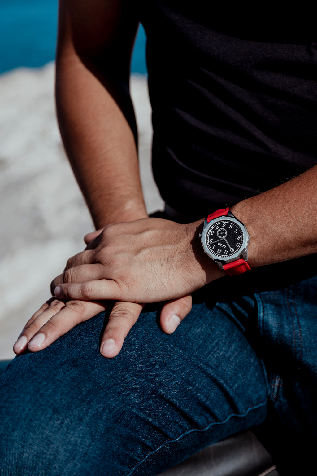 Homme assis portant la montre OURO RW-001 avec le bracelet sport rouge perforé en silicone.