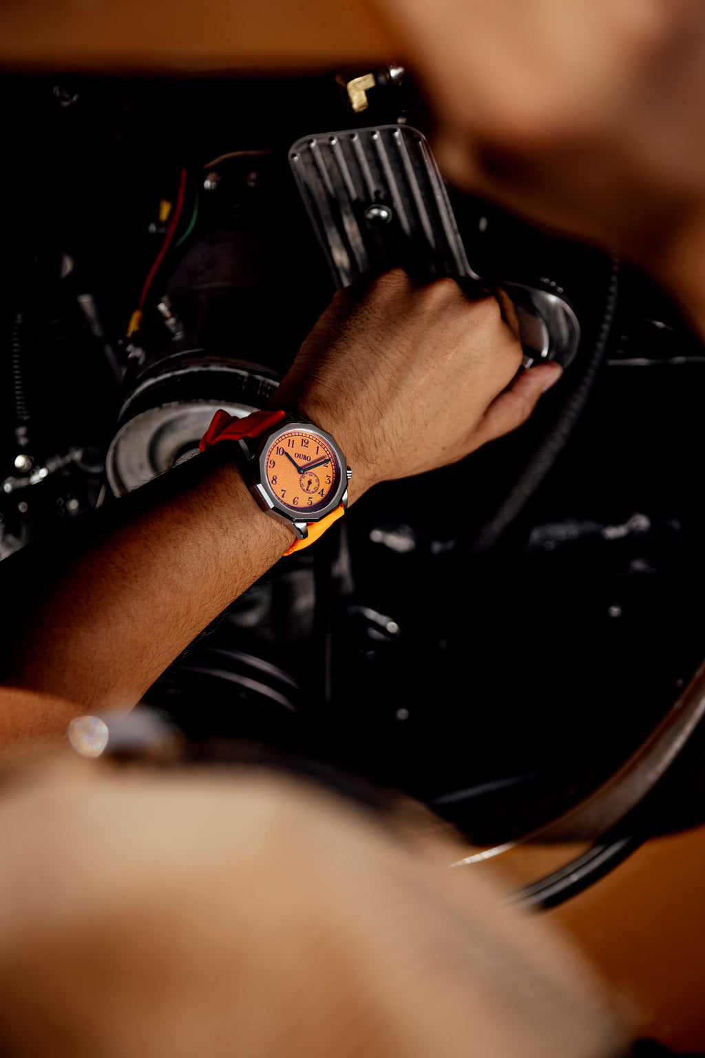 Montre OURO RW-003 avec bracelet sport en silicone orange perforé porté au poignet d’un conducteur vérifiant son moteur.