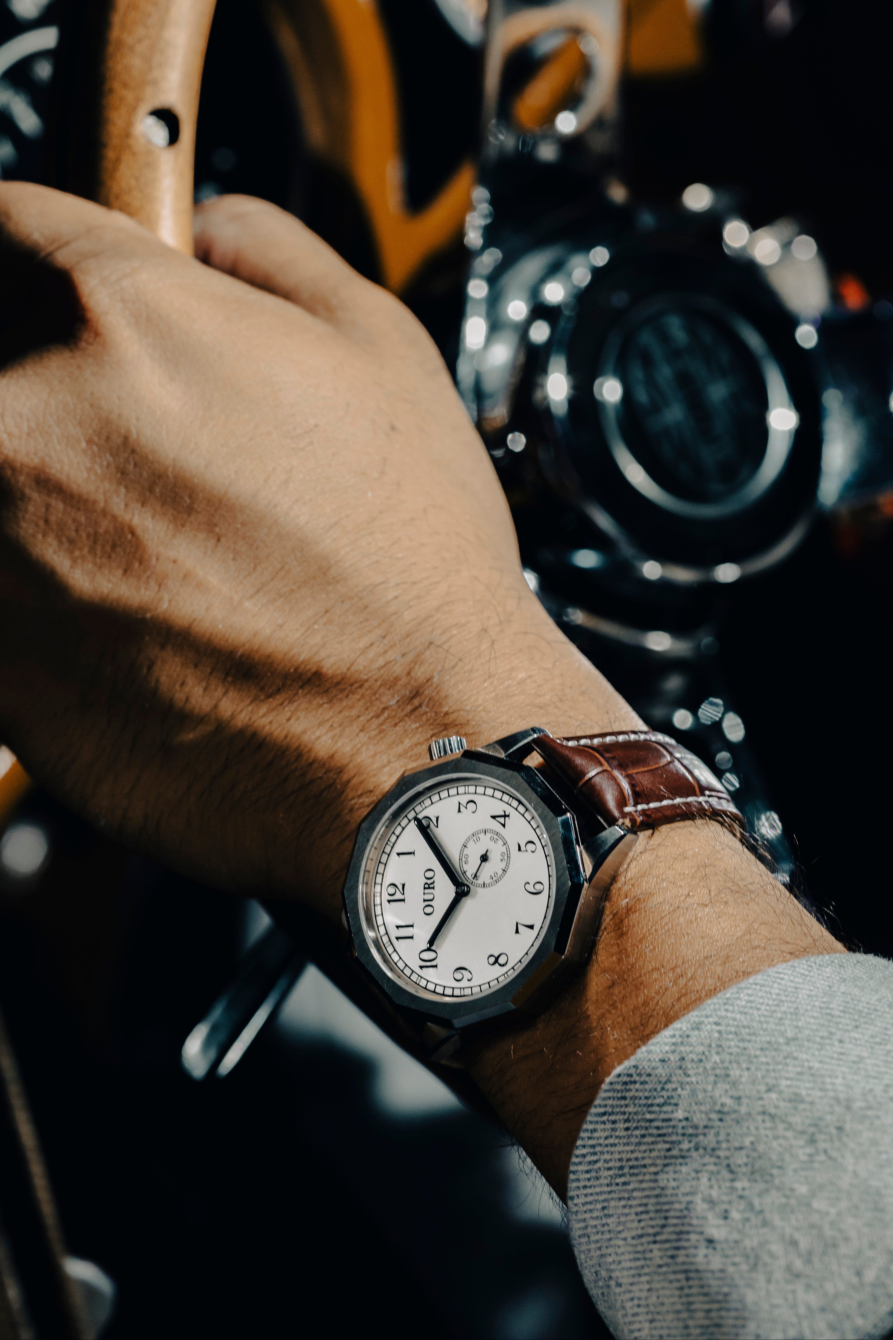 Gros plan sur la Driver’s watch RW-002 à cadran inox brossé associée au bracelet Grand Tourisme en cuir marron embossé crocodile et à surpiqûres blanche portée au poignet.
