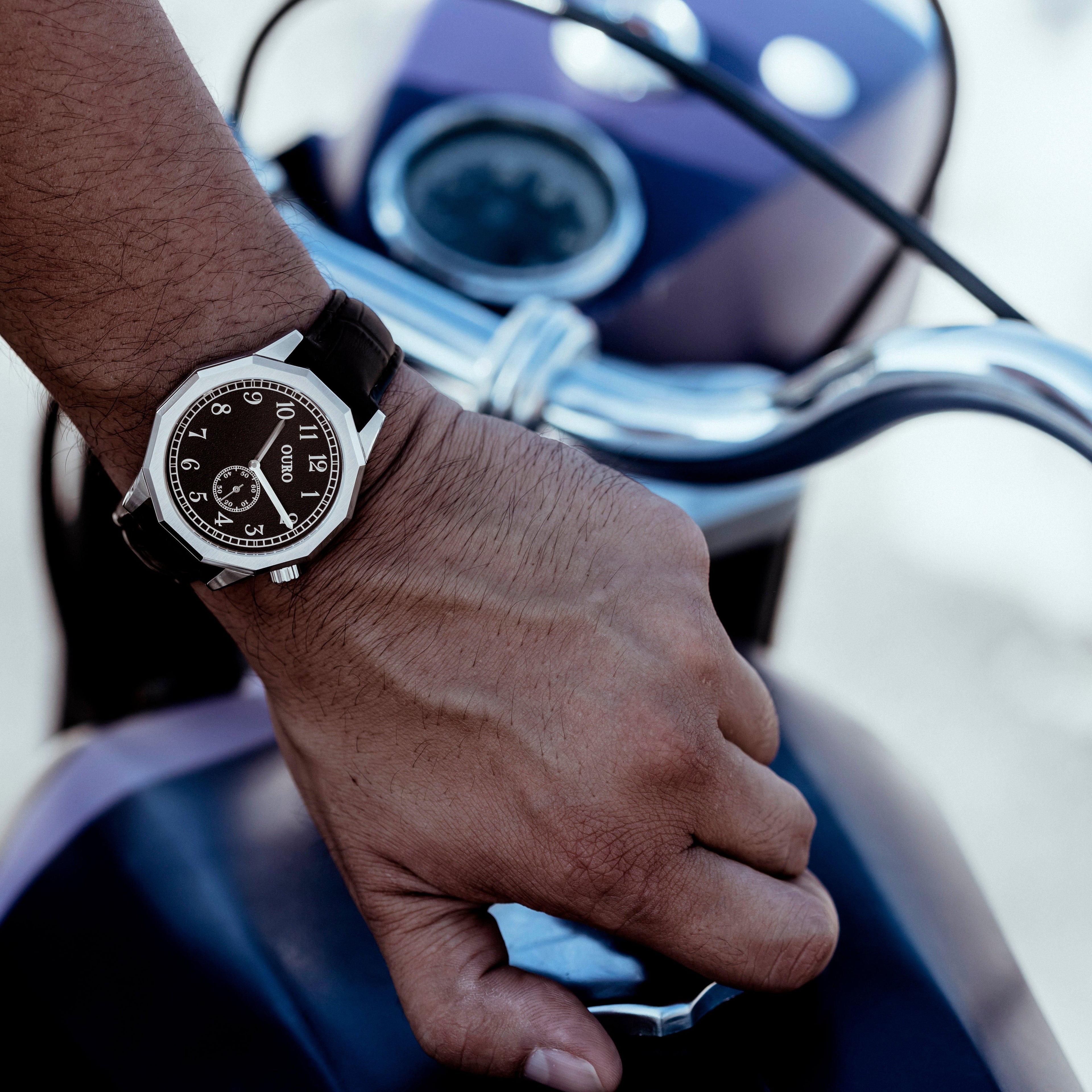 Driver’s watch OURO RW-001 cadran noir décalé à 45° au poignet d’un motard ouvrant le bouchon de réservoir d’une moto vintage.