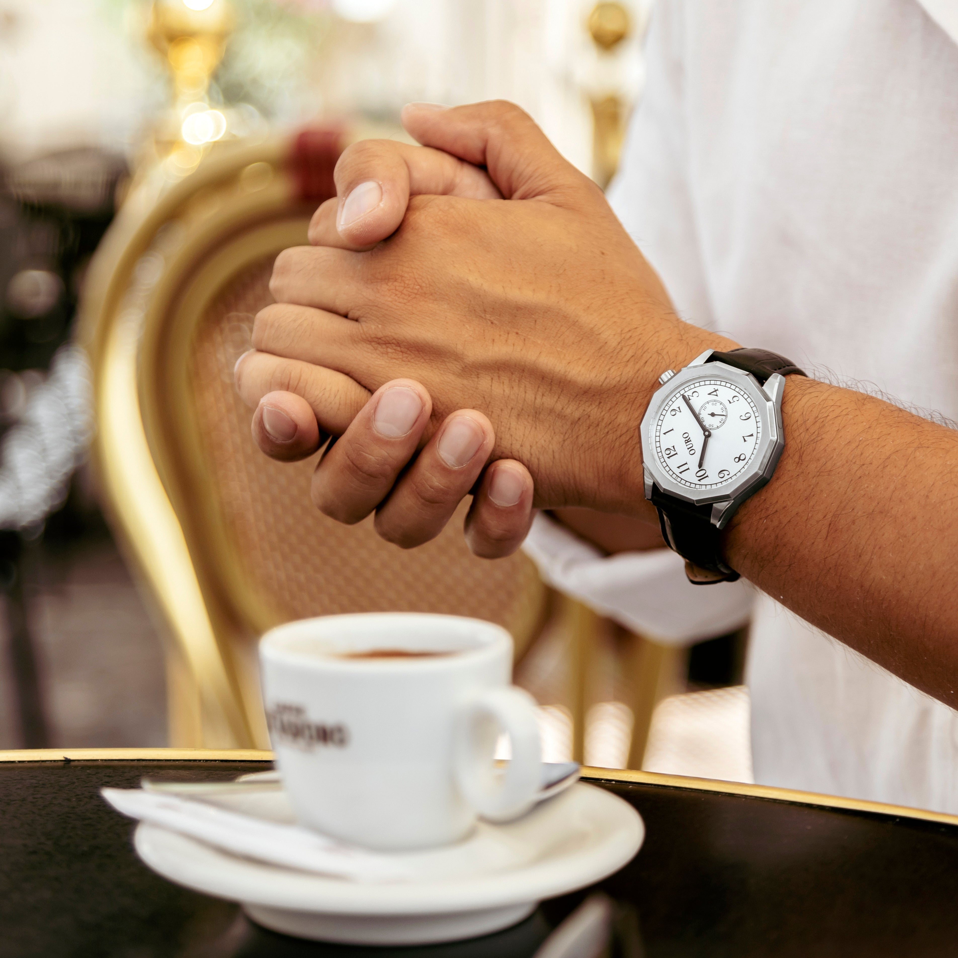 Montre OURO RW-002 cadran inox brossé décalé à 45° au poignet d’un homme prenant un café assis en terrasse.