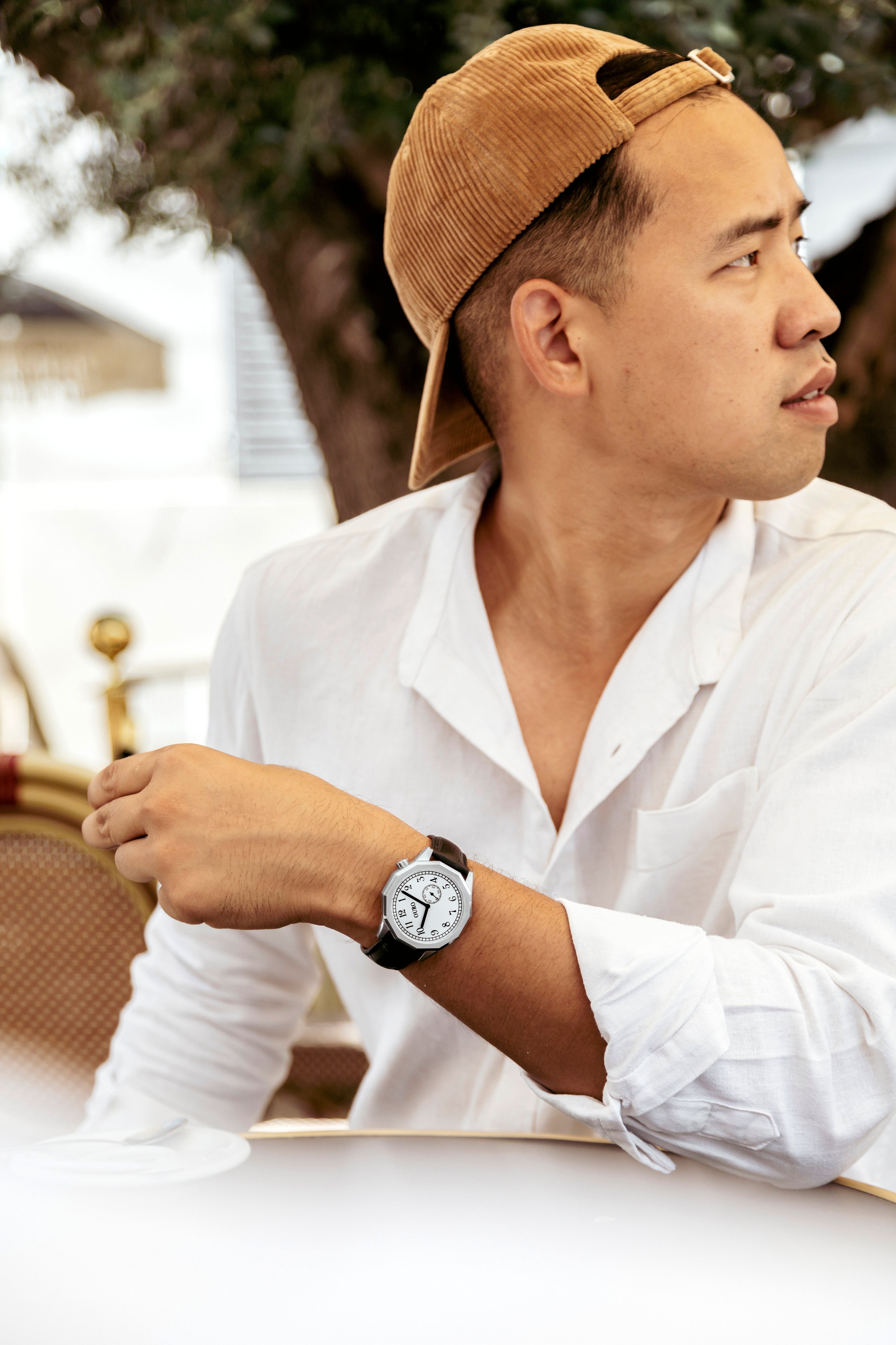 Montre OURO RW-002 cadran inox brossé décalé à 45° au poignet d’un homme en chemise blanche installé à une table de terrasse de café.
