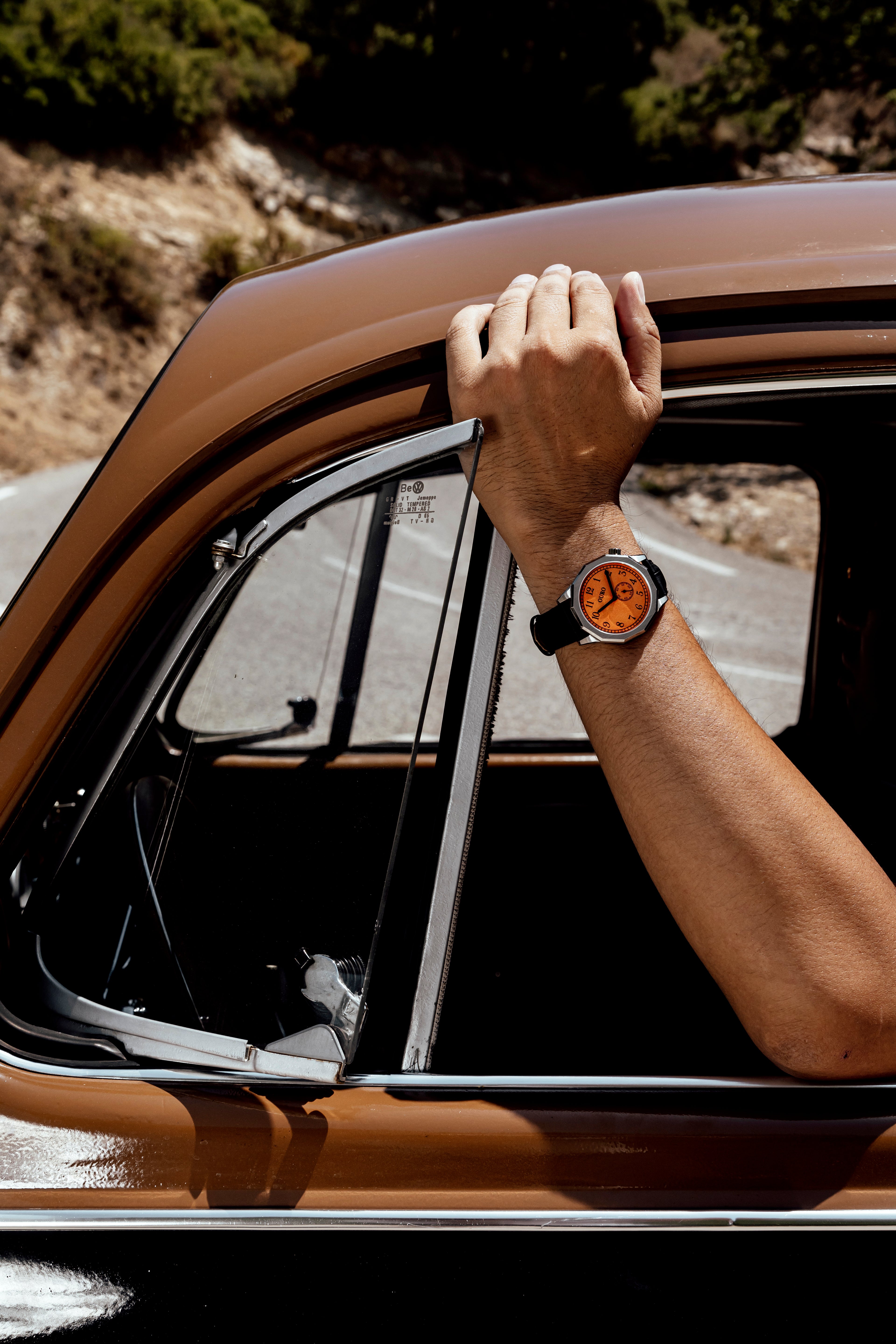 Driver’s watch OURO RW-003 cadran orange décalé à 45° au poignet d’un conducteur le bras à la fenêtre.