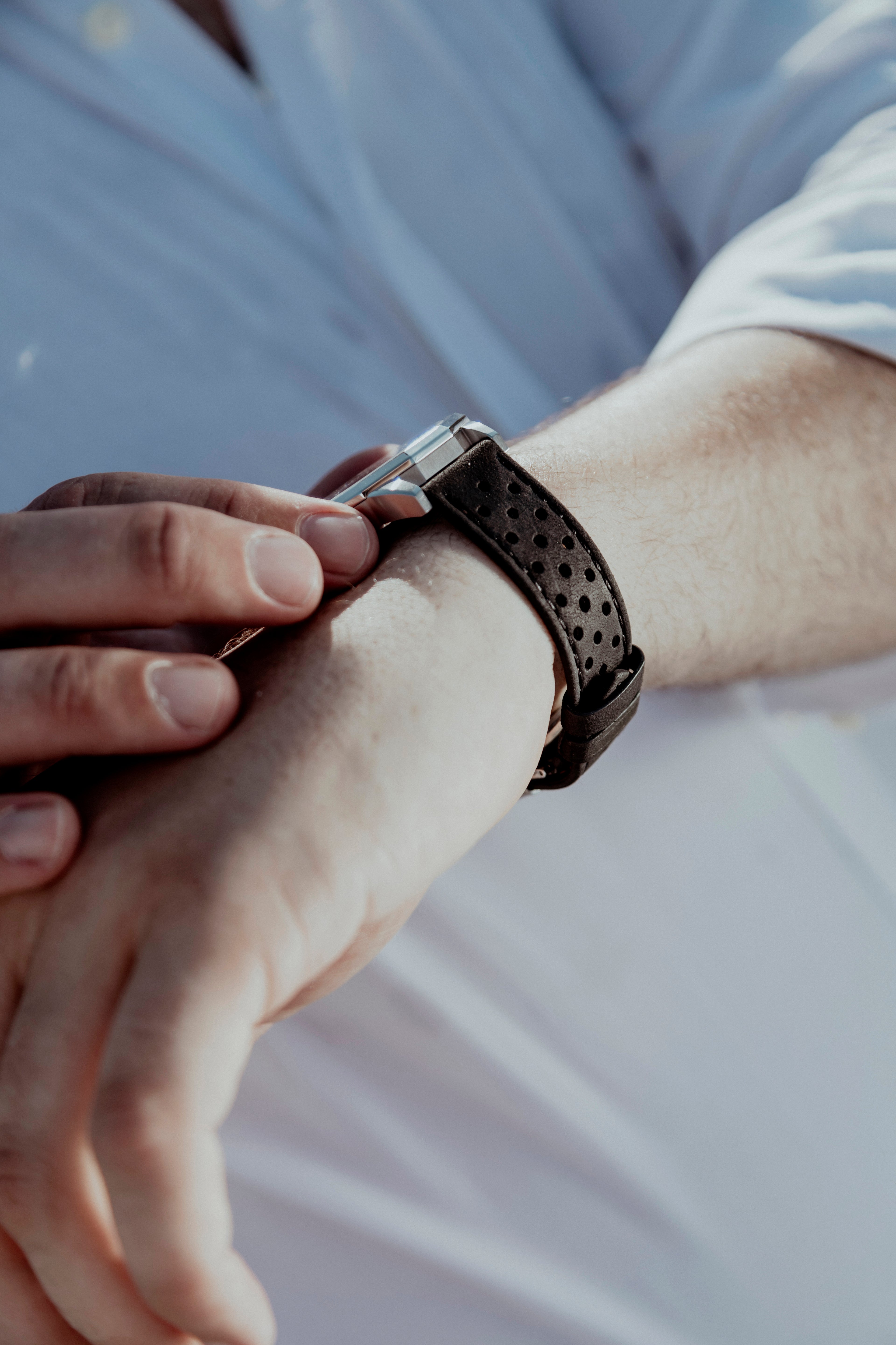 Gros plan sur le bracelet Rallye noir mat perforé associé à une montre OURO portée au poignet.