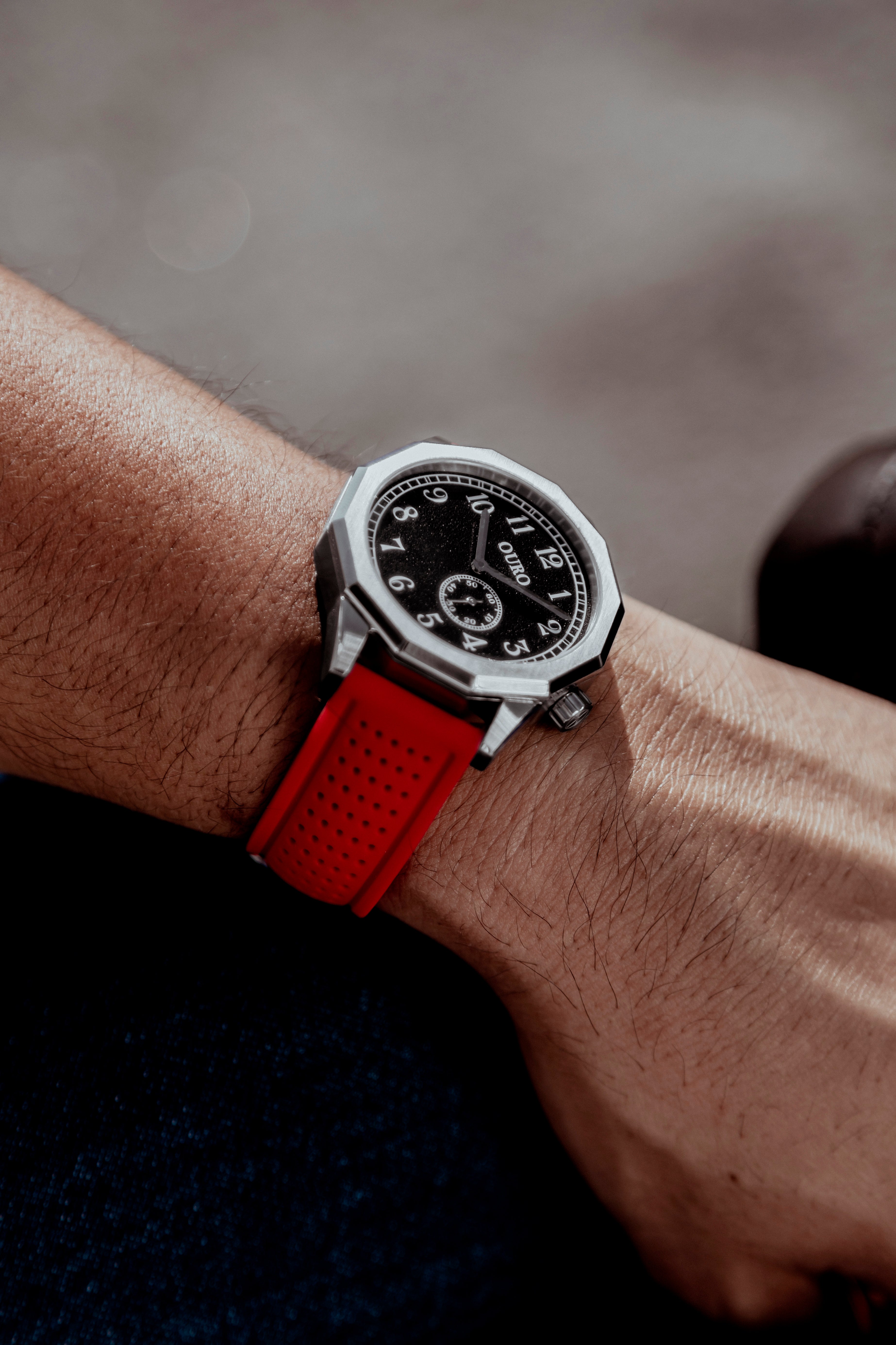 Gros plan sur la Driver’s watch RW-001 à cadran noir grainé associée au bracelet Sport en silicone rouge perforé portée au poignet.